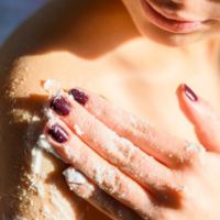 A close-up of a person exfoliating their shoulder with a scrub, focusing on their hand