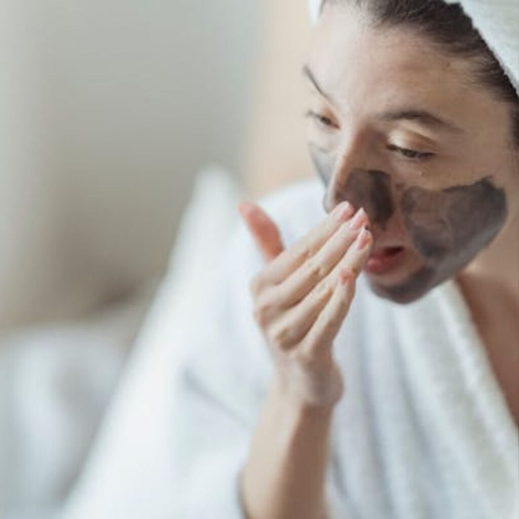 Close-up of a woman applying a charcoal face mask, highlighting a natural skincare routine in a calming setting.